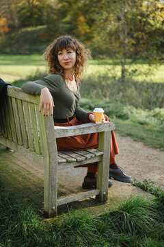 Stylish woman enjoying coffee on a park bench