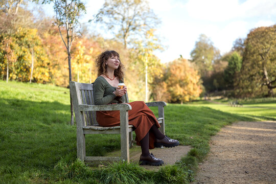 Woman enjoying coffee on a park bench in autumn