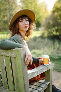 Woman in a hat enjoys her coffee on a park bench