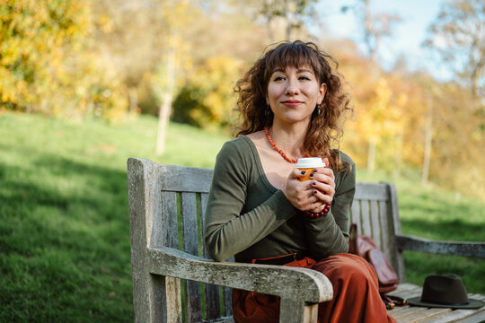 Woman relaxing on a park bench with coffee, copy space