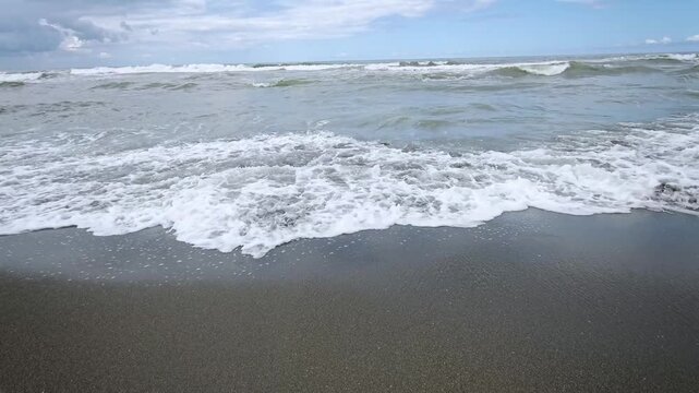 Rough Sea Waves Rolling onto Empty Dark Sand Shoreline on Cloudy Day