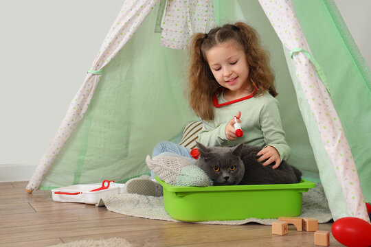 Cute little girl with first aid kit giving injection to her British cat in hovel at home