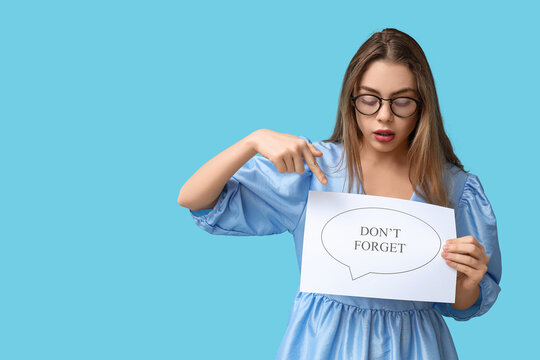 Young woman pointing at speech bubble with text DONT FORGET on blue background. Reminder concept