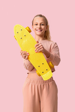Happy teenager girl with skateboard on pink background