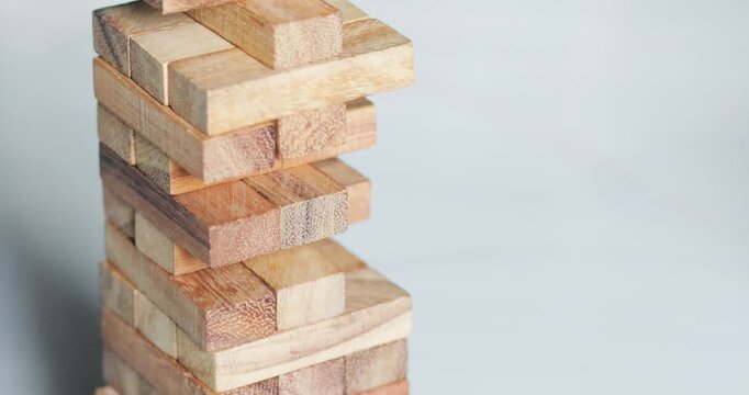 Hand removing a wooden block from a stacking tower game, strategy, decision making, risk, balance, problem solving, teamwork, and business concepts, close-up