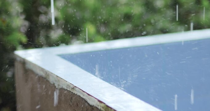 Raindrops splashing on a cement basin edge with a blurred green background. Fresh rainy atmosphere, perfect for weather, nature, seasonal and background