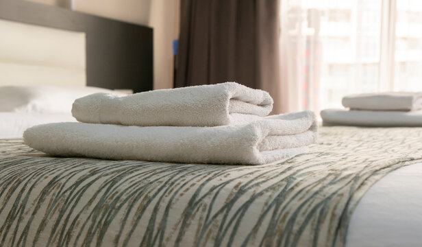 Clean towels stacked neatly on a bed in a hotel room during daylight