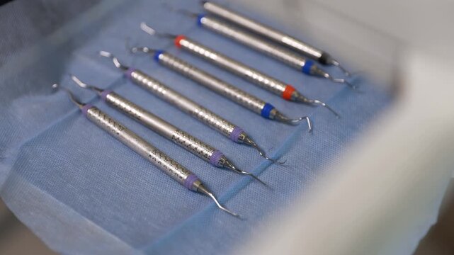 Gloved hand selecting dental scalers and explorers beside blue sterile drape on clinical tray, viewed from low diagonal angle with polished metal tips and organized instrument layout