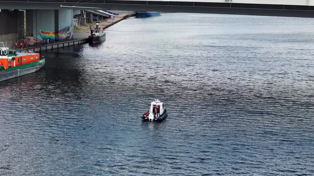 A police patrol boat moves on the Odra river in Szczecin, Poland, with a wide panorama of the city bridge, traffic, and historic architecture.