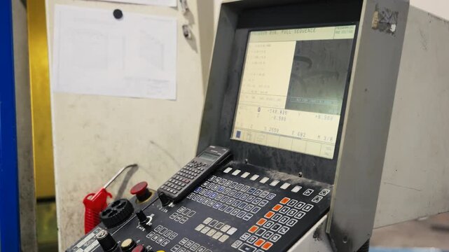 Close up of an industrial CNC machine control panel monitor displaying programming sequence code and keypad in a manufacturing factory