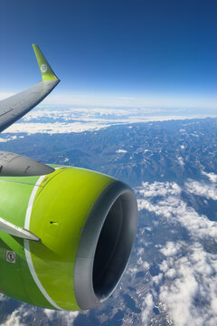 Novosibirsk, Russia - 22 июля  2026г: Airplane Wing and Engine Airline companies S7 above Mountain Range During Flight Under Blue Sky.