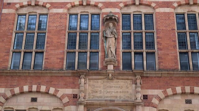 Front facade of a red brick church institute building with a central religious statue and tall mullioned windows.