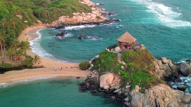 A smooth forward shot approaches the famous thatched-roof gazebo atop a rocky headland in Tayrona National Park, Colombia.