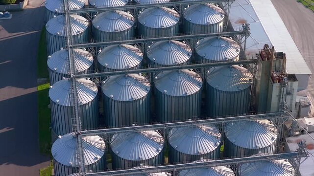 Top down aerial view zooming in on large silver grain elevators at a modern agro processing plant, highlighting industrial farming and food production