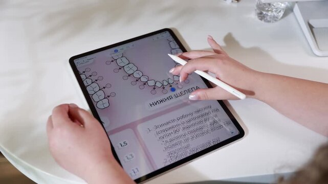 Hands with stylus annotating dental diagram on tablet during telemedicine consultation, showing close interaction with medical interface, color chart, white workspace