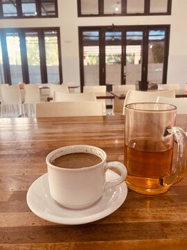 Cozy coffee and tea sit on rustic wooden table
Cozy coffee and tea sit on rustic wooden table. Empty cafe space frames the warm beverage setup. Soft light filters through tall glass windows. Calm, inv