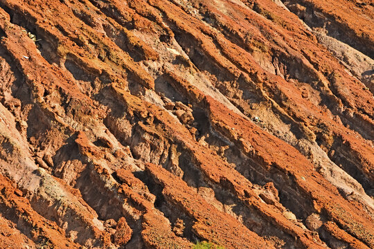 A close-up detail of heavily eroded reddish-orange soil showing deep gullies and ridges caused by mining activities in Lefke.