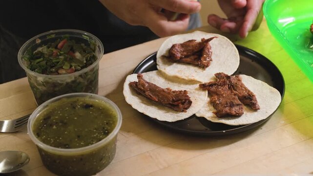 Close up cooking footage showing man making arrachera steak tacos topped off with green salsa and nopales while preparing homemade arrachera steak tacos in a home kitchen