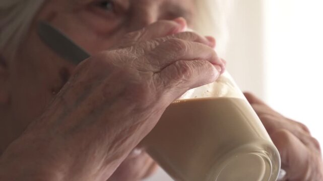 Close up of senior woman holding glass to drink liquid nutritional supplement at home