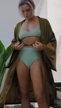 Elegant woman wearing luxury kimono robe over  swimsuit in modern tropical villa.