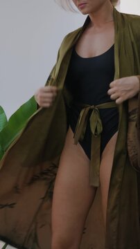 Elegant woman wearing luxury kimono robe over  swimsuit in modern tropical villa.