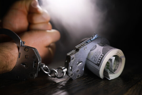 Hands of a fraudster with handcuffs on a background of us dollars. Fraud, cyber crime concept. Arrest of an entrepreneur in the workplace.