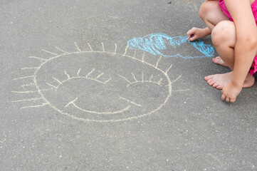 Little girl drawing a sun on the asphalt. The concept of children's creativity. © Alina Yermakova