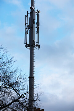 Tall Communication Tower Against Cloudy Sky with Tree in Foreground - Stock Photography