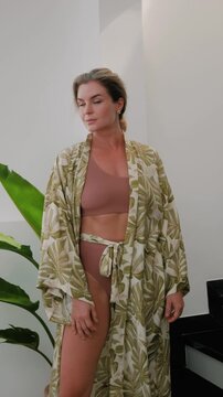 Elegant woman wearing luxury kimono robe over  swimsuit in modern tropical villa.