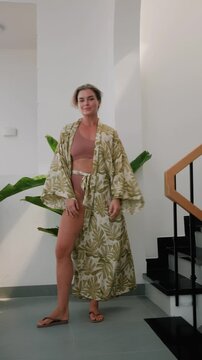Elegant woman wearing luxury kimono robe over  swimsuit in modern tropical villa.