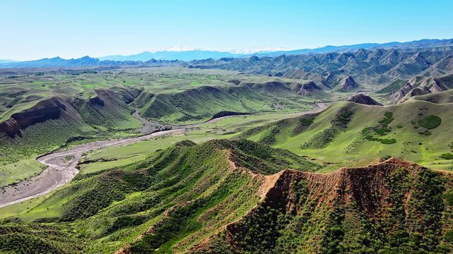 Aerial view of a green mountain valley with a winding riverbed under a blue sky along the scenic S101 highway in Xinjiang, China