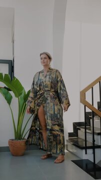 Elegant woman wearing luxury kimono robe in modern tropical home.
