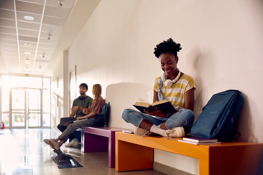 Happy black female student learning from book.