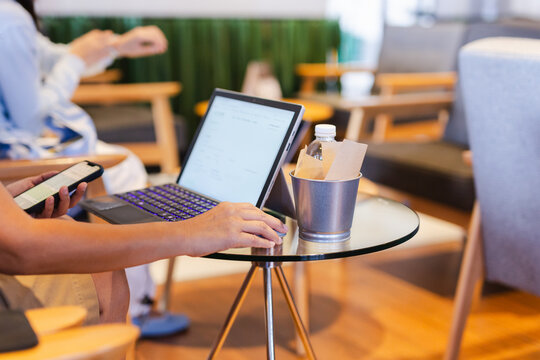 Business woman holding a smartphone while using a laptop  in co working lounge.