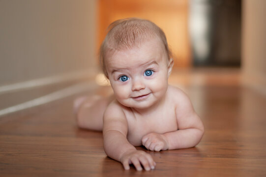 Cute blue eyed baby smiles on a hardwood floor