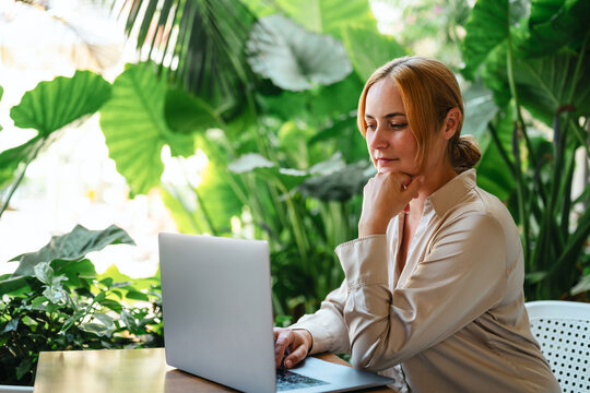 Pensive woman working on laptop surrounded by plants