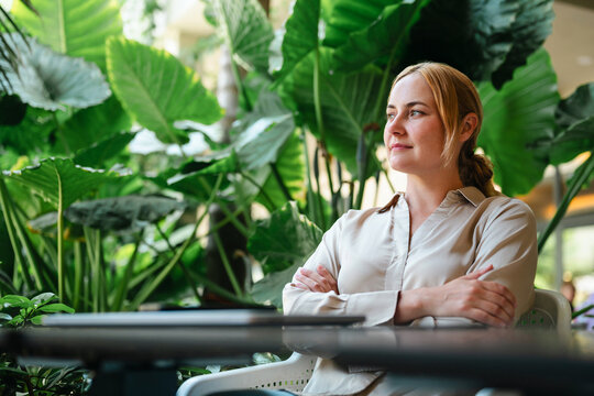 Thoughtful woman sits at table surrounded by lush plants