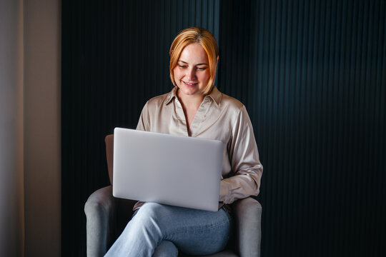 Smiling woman using a laptop in a chair, remotely work