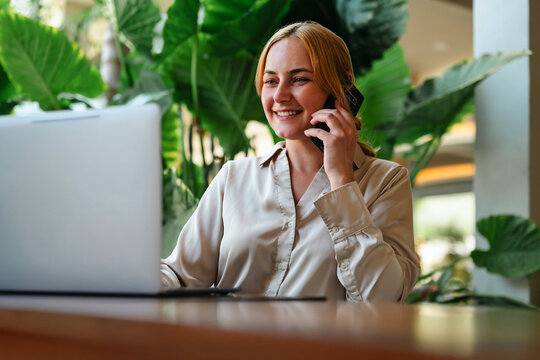 Smiling woman talking on her phone using laptop