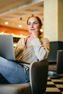 Thoughtful woman with laptop in modern lounge, remote work