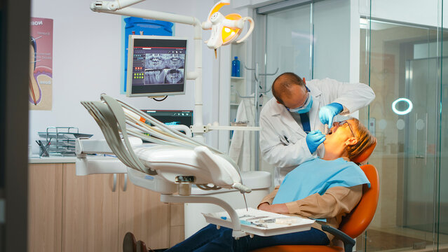 The inspection establishes the current condition of the teeth before any procedure as the dentist examines the woman patient's teeth with sterile instruments in a dental clinic.
