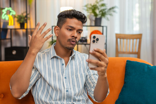 Indian man at home talks on online video call with friend laughs waves hello and shows good mood. Arabian guy on sofa says bye shows ok gesture near camera and smiles while ending call after fun talk
