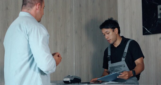 Customer making credit card payment on terminal with staff at car repair service counter