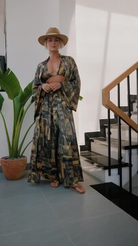 Woman modeling flowing patterned resort wear with bikini top and wide leg pants in bright modern interior.