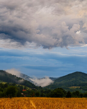 Heavy clouds and low mist lingering over rolling green mountain ridges under a vast blue sky