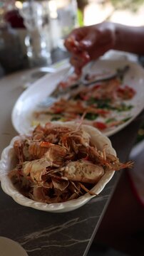 Vertical screen woman eats grilled langoustines with her hands at a restaurant table separating tender seafood meat from shells during a relaxed summer meal
