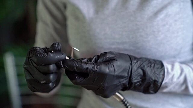 Black nitrile gloved hands assembling rotary handpiece with metal bit in workshop close-up, showing careful alignment, tightening, and precise maintenance under soft directional light