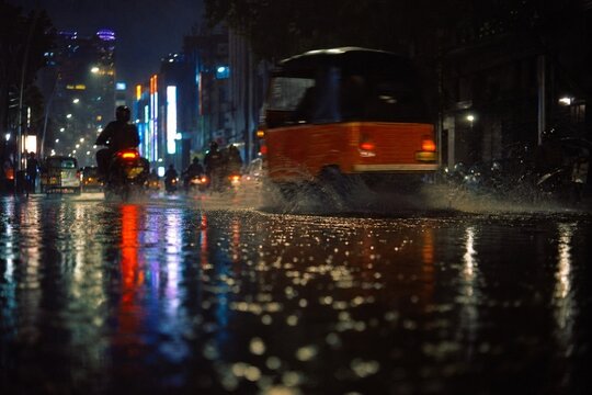 Rainy night in Jakarta with neon lights reflecting on wet asphalt as bajaj passes by