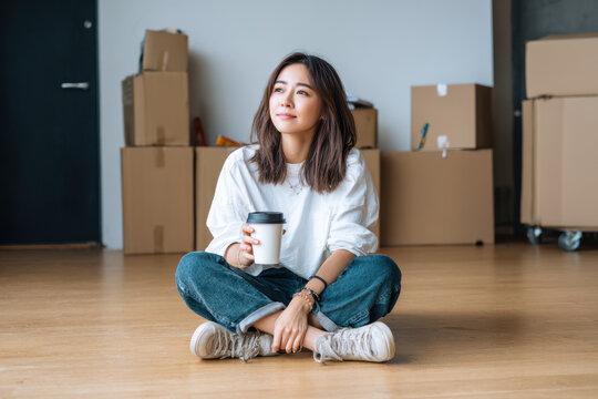 Asian woman enjoying coffee break while unpacking boxes after moving into new home