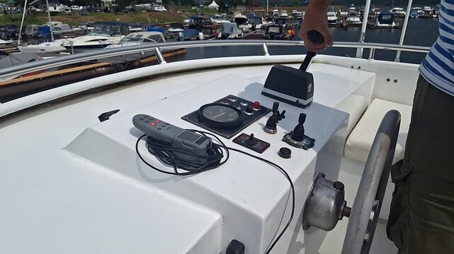 Male operator adjusts control panel on boat deck, manipulating switches and dials while moored at marina with various boats in the background